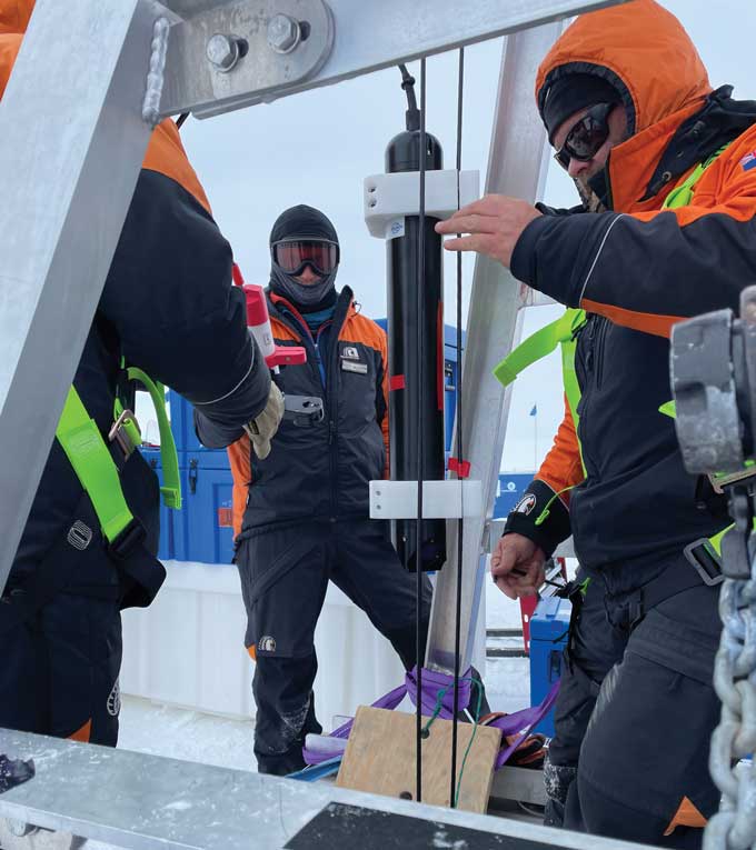 Three men in heavy winter weather gear stand around a scientific instrument.